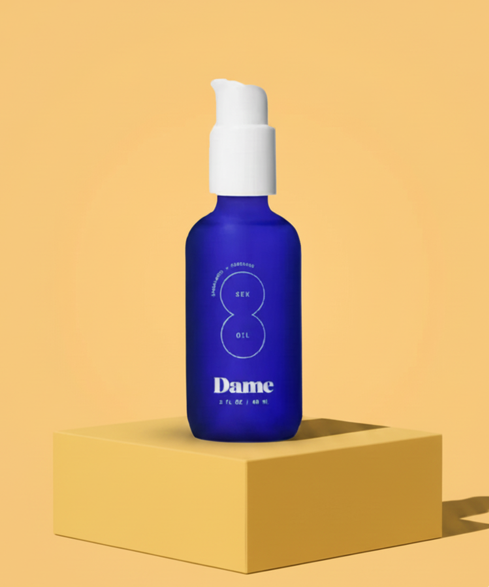 Bottle of Dame Oil-Based personal lubricant with white cap on a beige background