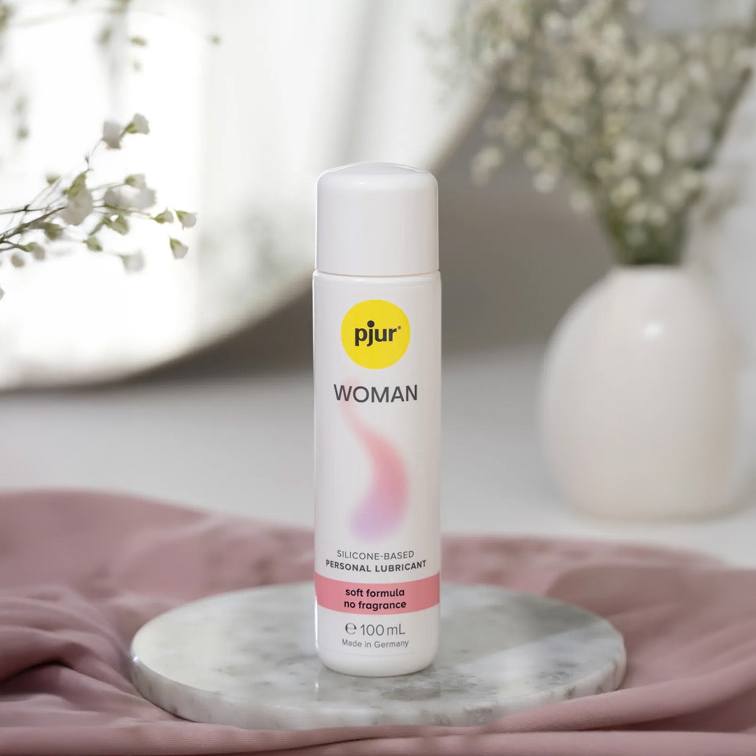 Pjur Woman silicone-based personal lubricant bottle on a marble coaster with flowers in the background